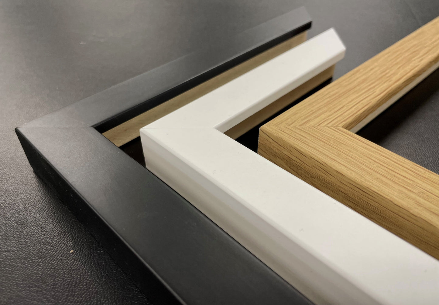 three different types of frames or borders, including a black frame, a white frame, and a wooden frame, arranged on a dark surface.